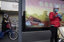 Žena v roušce stojí 13. dubna 2020 před plakátem, na kterém je zobrazena Brána nebeského klidu (Tchien-an-men)