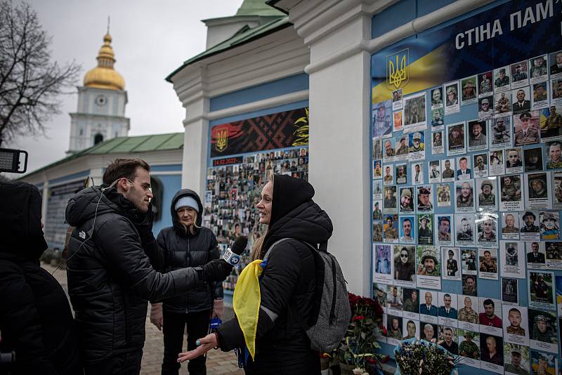 Žena dává rozhovor do televize před zdí padlých obránců Ukrajiny v rusko-ukrajinské válce před katedrálou svatého Michala, 24. února 2023, Kyjev, Ukrajina.