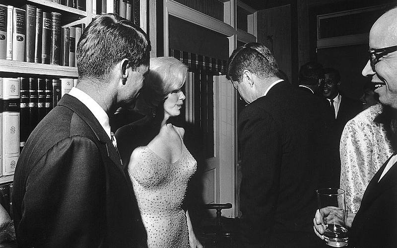 John F. Kennedy měl prokazatelně velké množství milenek, podle všeho se k nim řadila i herečka Marylin Monroe. Na snímku v ikonických šatech, ve kterých pro Kennedyho zazpívala píseň Happy Birthday, Mr. President. Vlevo Robert Kennedy.
