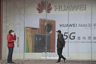 Lidé v rouškách před reklamním billboardem společnosti Huawei v Pekingu