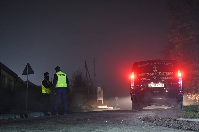 Vůz pohřební služby zaparkovaný vedle dvou policistů, kteří zajišťují přístup na místo výbuchu ve vesnici Przewodów.