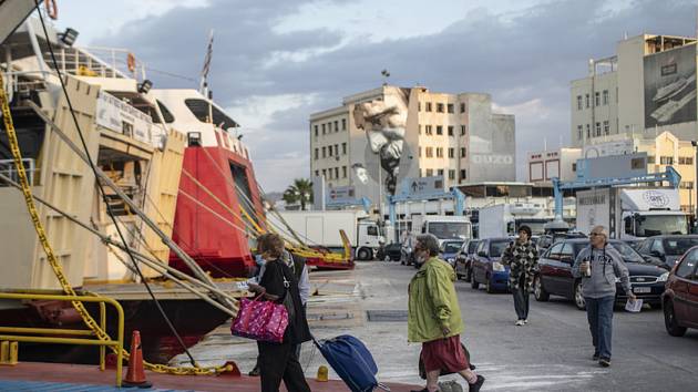 Lidé v rouškách nastupují na palubu trajektu v řeckém přístavu Pireus