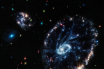 Velká galaxie připomínající kolo od vozu. Doprovází ji dvě menší spirální galaxie přibližně stejné velikosti