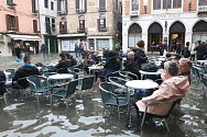 Turisté a místní obyvatelé sedí ve venkovní části restaurace na zaplavené ulici v italských Benátkách