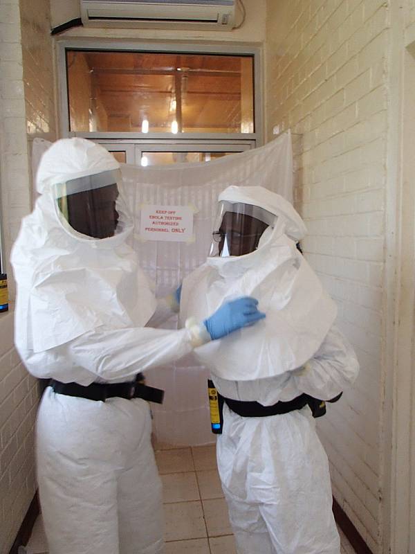 Liberijští laboranti Aaron Momolu (vlevo) a Lawrence Fakoli si před vstupem do uzavřeného prostoru pro testování vzorků nasadili ochrannou výstroj