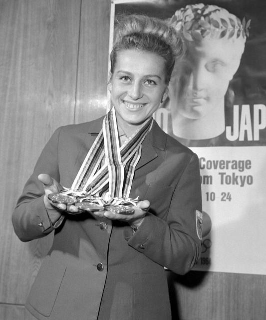 Portrét trojnásobné olympijské vítězky v gymnastice Věry Čáslavské drží olympijské medaile z Tokia.
