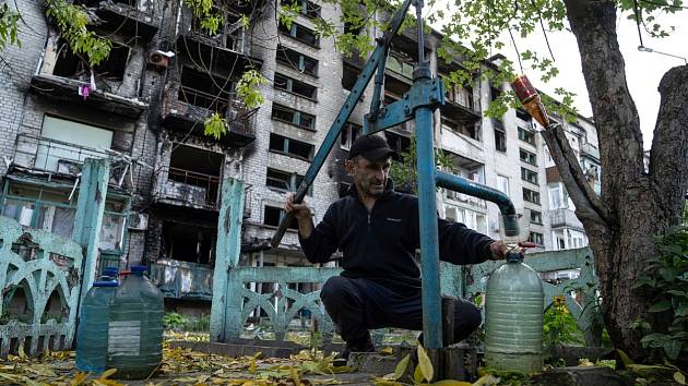Ukrajinský civilista pumpuje vodu před zničenou obytnou budovou v Ukrajinci osvobozeném Lymanu
