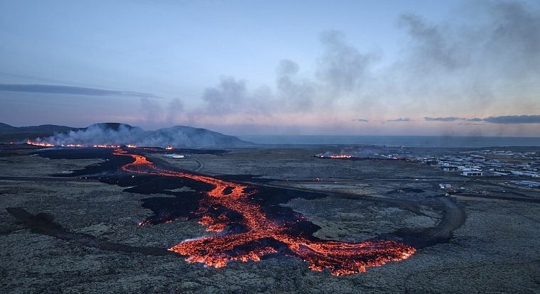 Výbuchy lávy a valící se kouř jsou vidět poblíž obytných budov v jihozápadním islandském městě Grindavík po sopečné erupci dne 14. ledna 2024.