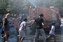 Lidé se v horkém počasí osvěžují ve vodní spršce z kropicího vozu na Staroměstském náměstí v Praze
