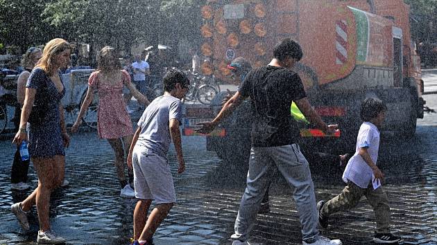 Lidé se v horkém počasí osvěžují ve vodní spršce z kropicího vozu na Staroměstském náměstí v Praze
