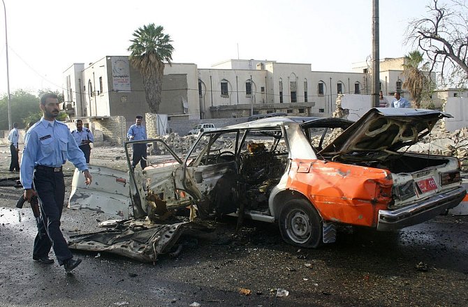Irácký policista prochází kolem zdemolovaného auta na místě výbuchu v jihoiráckém městě Basra 21. dubna 2004. Více než šedesát lidí bylo při explozi zabito a asi sto zraněno.