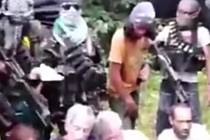 Rukojmí na videonahrávce sedí na trávě uprostřed džungle a jsou obklopeni více než desítkou většinou maskovaných ozbrojenců. 