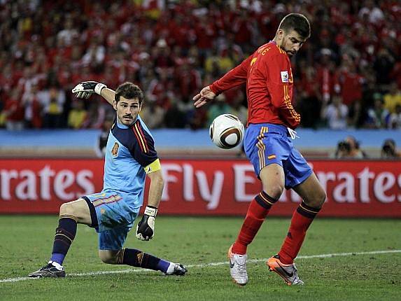 Gólman Španělska Iker Casillas a Gerard Pique sledují míč, který míří do jejich sítě.