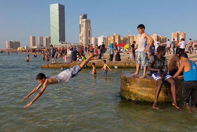 V ospalém pátečním dnu se chlapci zchlazují na pláži v Tripolisu. S obnovou normálního života Libyjci doufají, že hotely jako Marriott (zelená budova vlevo) se znovu otevřou pro rodící se turistický r