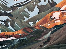 První paprsky červnového dne osvětlují hřbet sopečného ryolitu, rezavě zbarvené vulkanické horniny v Landmannalaugaru. 