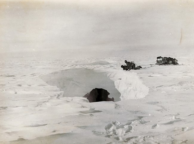 Posádka saní nahlíží do ledovcové pukliny chvíli před neštěstím. Družstvo Douglase Mawsona překonalo mnoho hlubokých puklin, než v jedné z nich zmizel Belgrave Ninnis, šest psů a důležitá výbava včetn
