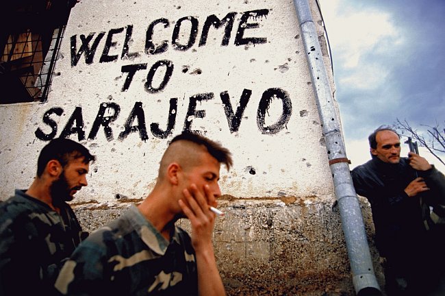 Bosensti Srbove kouří a odpočívají na frontové linii vedle nápisu Vítejte v Sarajevu. V zákopech se kolem Sarajeva bojovalo všude. 1994 