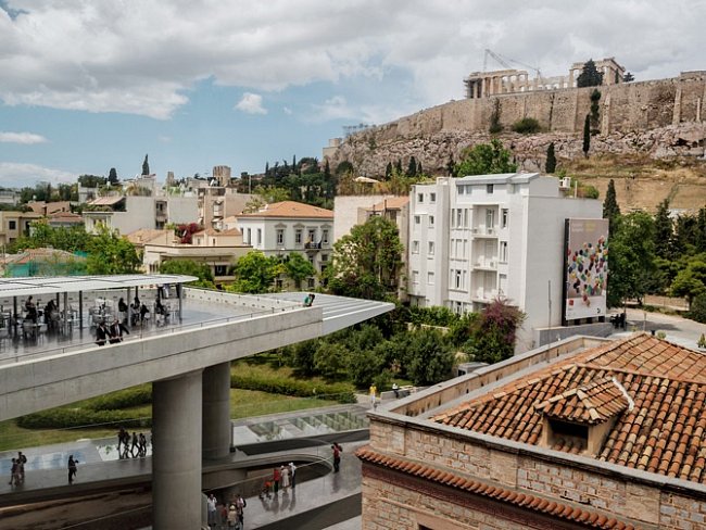 Moderní symbol národní hrdosti, muzeum Acropolis (vlevo), částečně financované z prostředků Evropské unie a dokončené roku 2007, vzhlíží k věhlasné řecké paměti­hodnosti − Parthenonu.