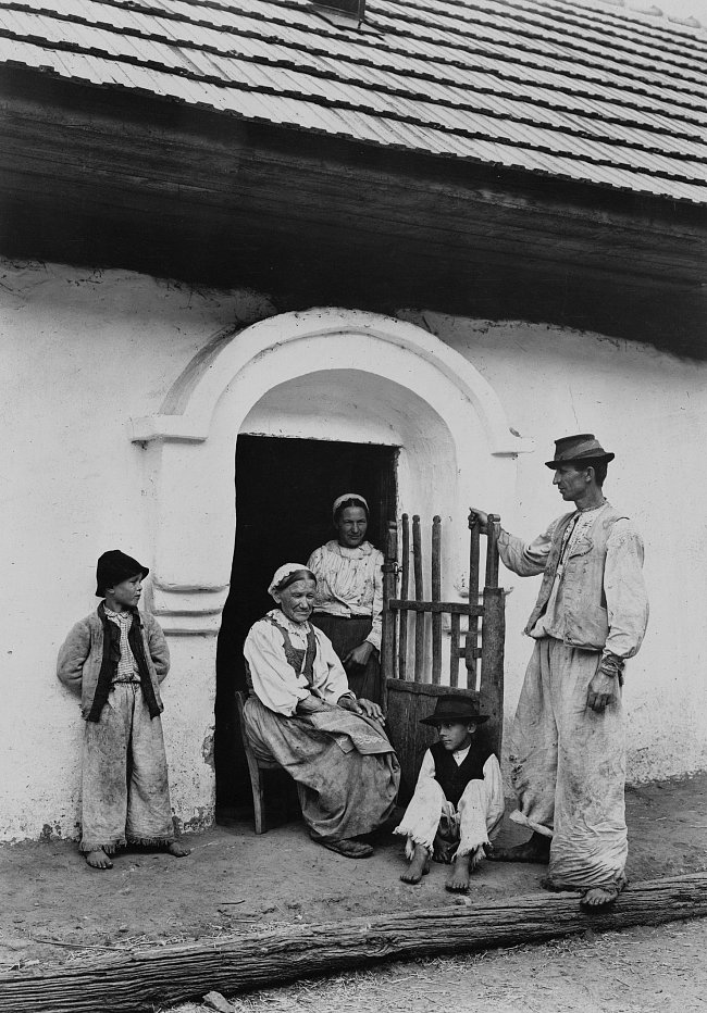 Slovenská rolnická rodina ve svém běžném oděvu
Povšimněte si oblouku v normanském stylu, který je pro slovenské domy typický. Povšimněte si také třásní dole na kalhotách, které jsou dosti široké opro