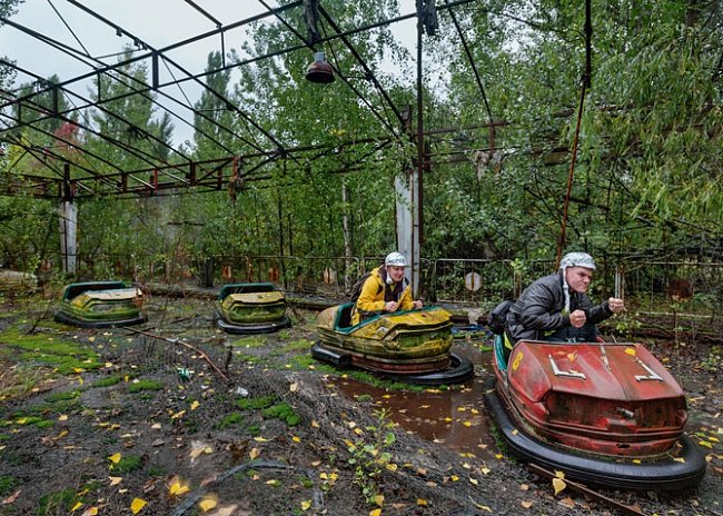Studenti z Finska, kteří mají pro pobavení i kvůli ochraně před deštěm na hlavě helmy z alobalu, pózují v autíčkách v zarostlém zábavním parku.