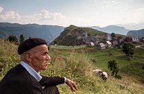 Bosna a Hercegovina: V Lukomiru žije 17 rodin a udržují se zde středověké tradice. Muž s cigaretou na fotografii odpočívá na kopci s výhledem na vesnici.