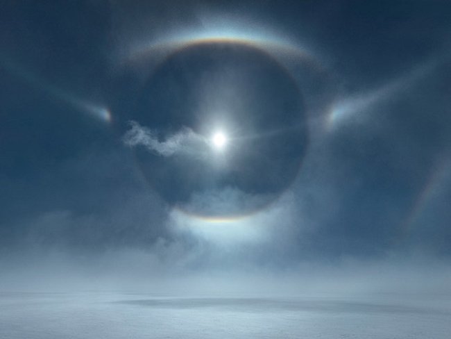 Soustava prstenců, kruhů a dalších halových jevů zářících nad ledovým příkrovem Grónska. Tyto jedinečné úkazy způsobuje lom slunečního světla na ledových krystalcích, které víří v silném větru, nazývaném v Grónsku piteraq.