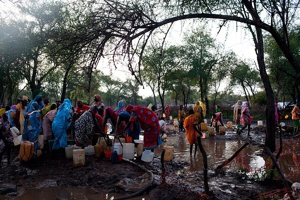 Ženy a děti se brodí vodou a bahnem, aby si naplnily své kanystry u distribučního místa pitné vody v táboře Batil. Silné deště a záplavy v táboře zhoršily už tak špatný stav vodních zdrojů a sanitace.