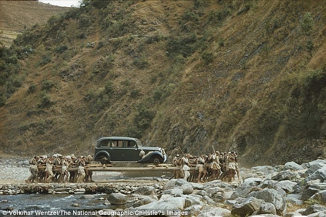 Snímek zachycuje nosiče, jak přenášejí auto přes řeku v Nepálu. 