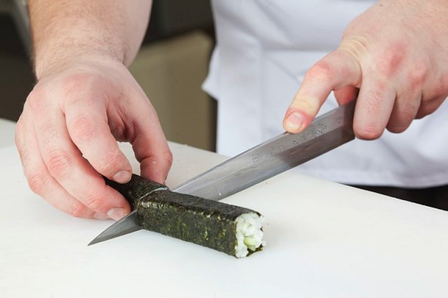 5. Pokud jste pokračovali správně, získali jste rolku, která se nerozpadá. Nyní ji budete krájet. Vezměte ostrý nůž, namočte ho do vody (jinak se vám na něj nalepí rýže a sushi si můžete zničit). Rolku rozkrojte v polovině a obě půlky ještě překrojte na 3
