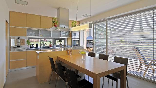 Kuchyně je zařízená v příjemných teplých barvách a je propojena s jídelnou, kterou tvoří velký dřevěný stůl a kožené židle.
