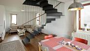 Lehké, zavěšené kovové schodiště pomyslně odděluje prostor obývacího pokoje od kuchyně a jídelny se vstupem na terasu.