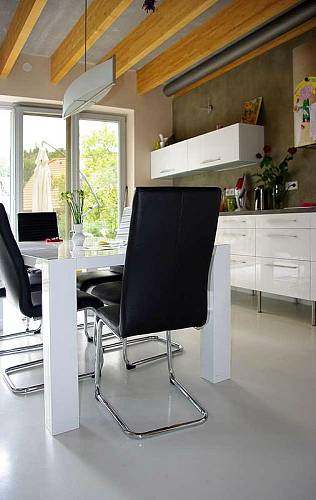 Součástí kuchyně je bílý leskle lakovaný jídelní stůl, ke kterému se usedá na pohodlné židle v černé barvě.