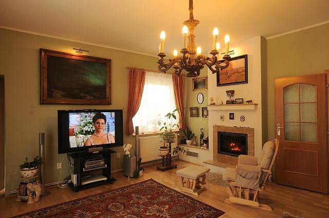 Obývací pokoj je vybavený perskými koberečky, krbem, velkoformátovými obrazy a dřevěným vyřezávaným lustrem.