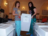 V zasedací síni Městského úřadu v Litoměřicích chystají  studentky střední školy volební urny pro jednotlivé volební okrsky.