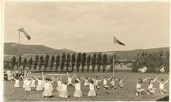 Vzpažit, upažit. Malá spartakiáda na obecním hřišti v červnu 1959. Děti cvičí na skladbu „Radostná jar“. V nádherném krajinném prostředí, díky kterému jsou Libochovany unikátní dodnes.