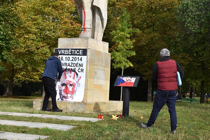 Aktivisté lepí plakát na podstavec sochy vojáka.