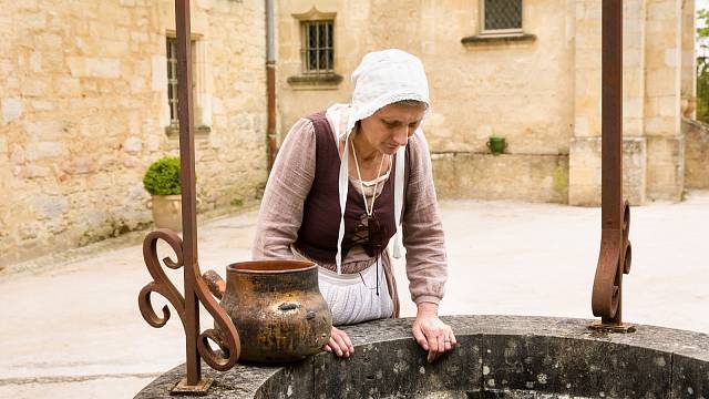 Žena v historickém oblečení pracující na staré vodní studně francouzského středověkého hradu