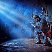 Středověký rytíř ve zbroji skládá přísahu věrnosti pokleknutím a skloněním hlavy k meči.