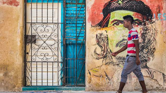 Mladý kubánský muž prochází kolem barevného portrétu Che Guevary namalovaného na omšelé staré zdi ve staré Havaně.