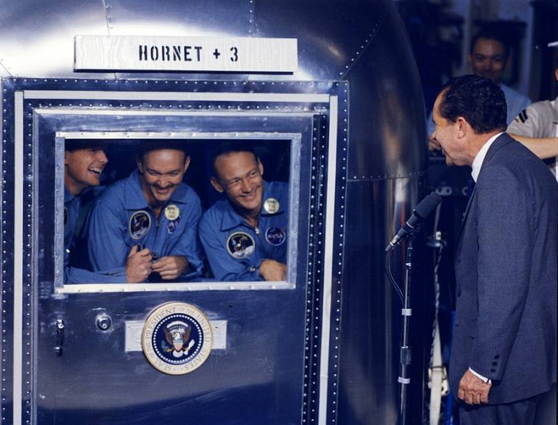 Armstrong, Collins a Aldrin se z izolačního kontejneru zdraví s prezidentem USA Richardem Nixonem. Propuštěni byli 17 dní po přistání.