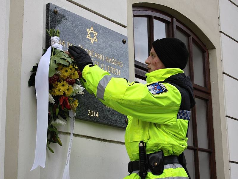 Strážník upevňuje květinu na pamětní desku na lounské synagoze