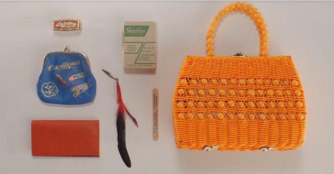 Obsah kabelky z roku 1976 - zrcátko s rtěnkou, pouzdro na make-up, přívěšek, šeková knížka, cigarety a pilníček na nehty