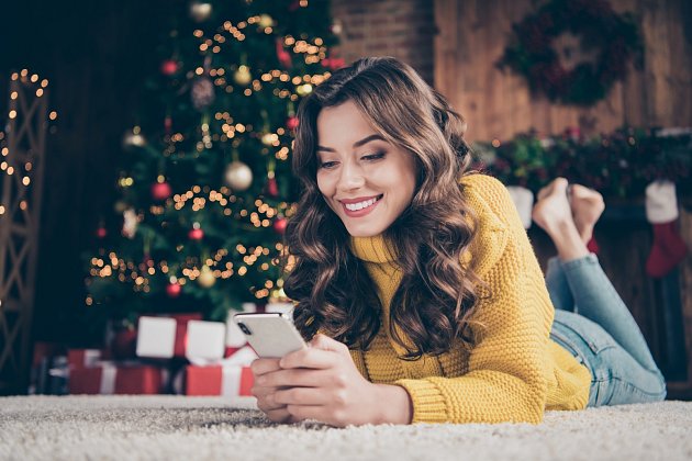 Dívka pod stromečkem s telefonem. Najděte si chvilku na vánoční SMS.
