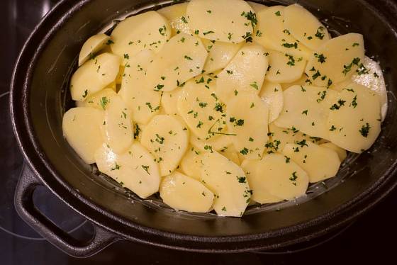 Oškrabané brambory nakrájíme na tenké plátky, skládáme je do pekáče, každou vrstvu osolíme a posypeme bylinkami.