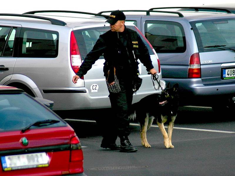 Policejní psovod prohledává okolí finančního úřadu.