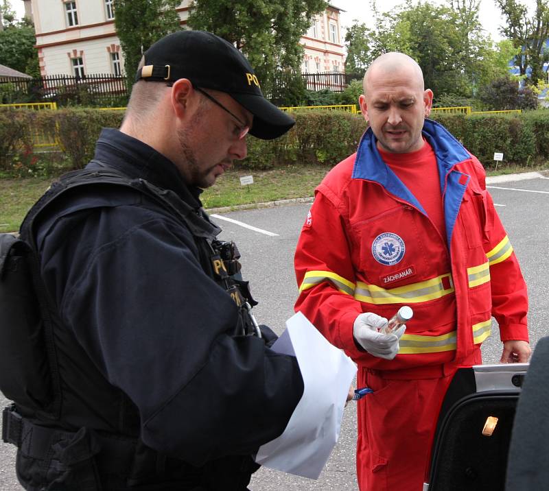 Záchranář předává policistovi placatku vodky