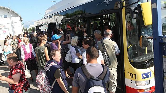 Lidé nastupují do autobusu na zastávce u nemocnice. Je na mostě, který teď město zavře, zastávka se přesune. 