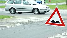 Značka upozorňující  na nerovnost vozovky varuje řidiče před propadlou silnicí před kruhovým objezdem.