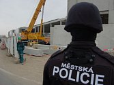 Strážník mostecké městské policie hlídá u brány na stavbu, aby někdo z nelegálně zaměstnaných neutekl. 