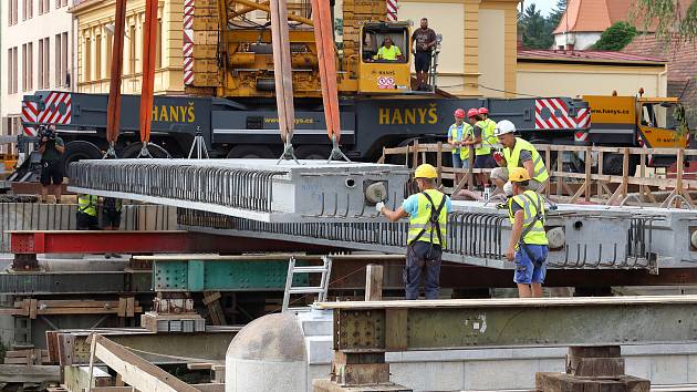 Největší kolový jeřáb v zemi v pondělí usadil na opravené pilíře deset betonových nosníků, z nichž se skládá nový most. Ten bude mít širší vozovku i vyšší nosnost. Řidiči se po něm projedou až příští rok.